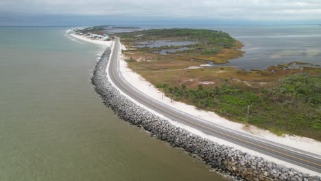 high aerial pull-away of waves crashing against rock barrier following road in cape san blas, florida