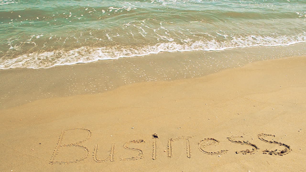 Indskrift 'business' i sand. Optagelse på stranden.