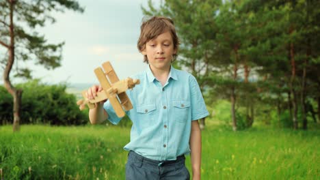 close-up view of happy little boy spinning and playing with wooden airplane toy in the park on a cloudy day