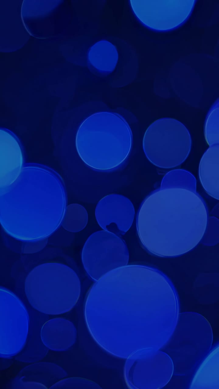 Sfondo video astratto con un'angolazione ravvicinata di cerchi bokeh blu fluttuanti su uno sfondo scuro.