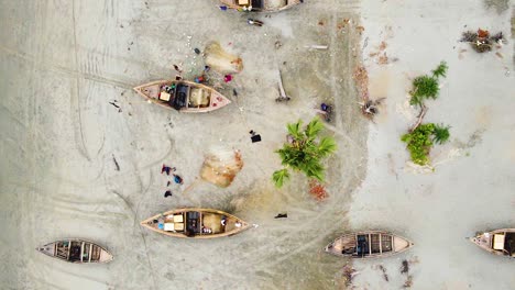 aerial view of fisherman repairing fish nets besides traditional wooden boats on kuakata sea beach, bangladesh