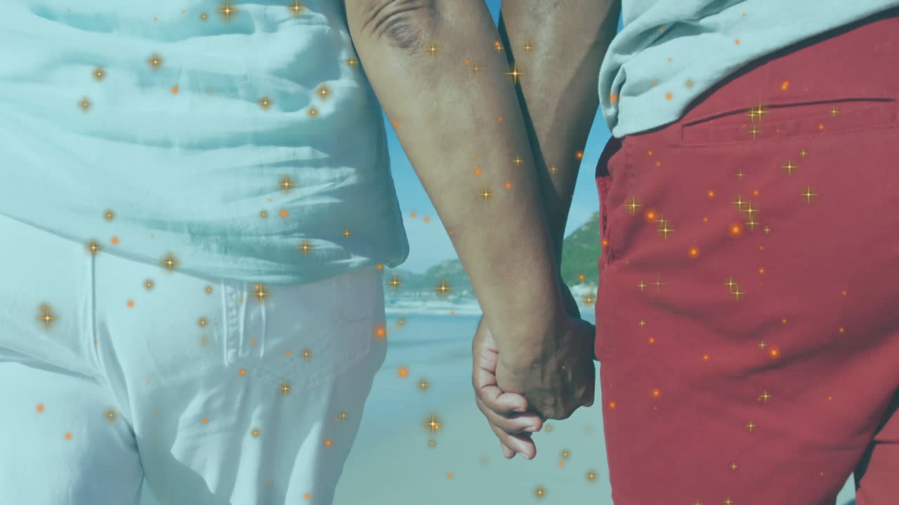 senior couple walking hand-in-hand on beach, with golden sparkles hovering for health marketing