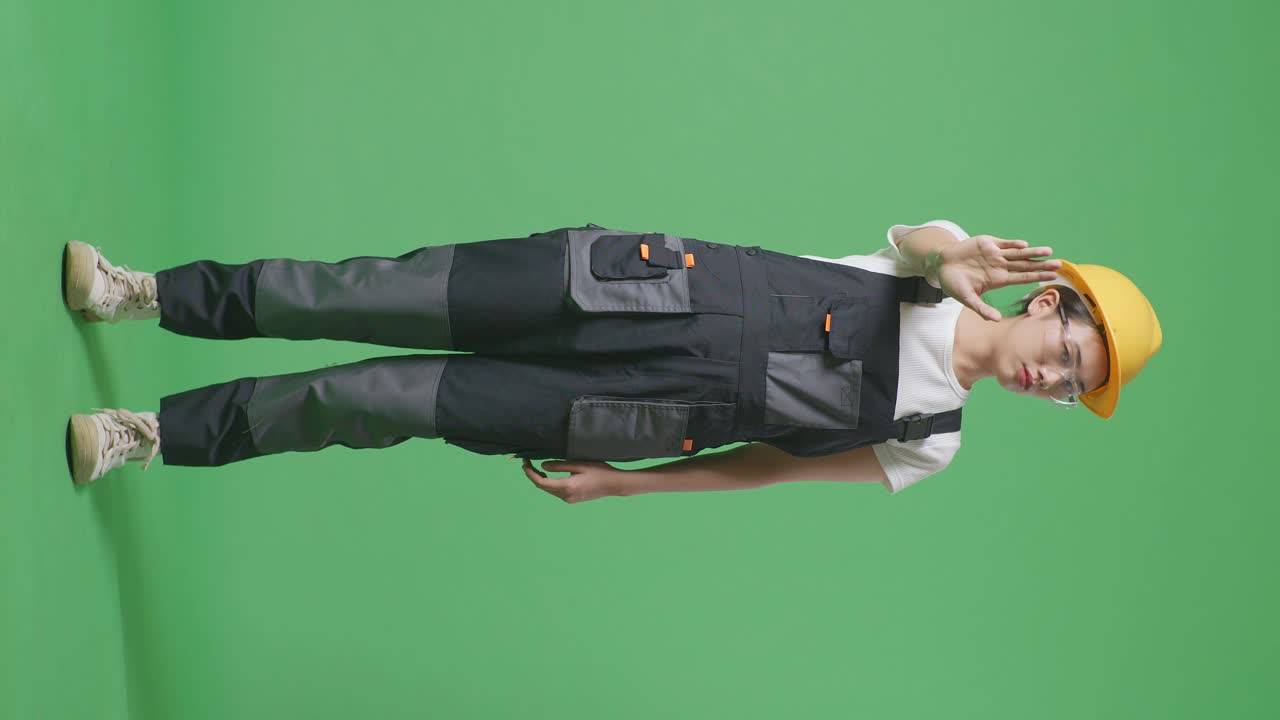 Full Body Of Asian Woman Worker Wearing Goggles And Safety Helmet Looking At Camera And Disapproving With No Hand Sign While Standing In The Green Screen Background Studio