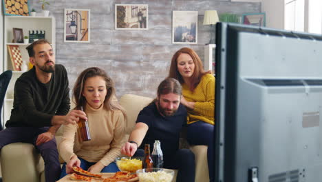 Man-reaching-for-his-beer-while-watching-tv