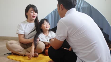 happy asian parents with daughter sitting in front of cloth tent at home while talking together