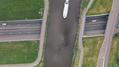 a luxemotor boat sails between two highway bridges over a dutch canal. zenithal zoom out shot on a clear day in netherlands