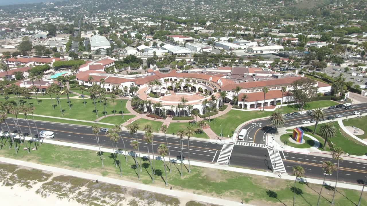 Circular aerial of a roman style building near the beach on Cabrillo boulevard during a warm and sunny day in Santa Barbara,California, USA. Cars are passing on the road, palm trees on the beach.
