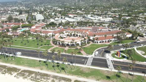 circular aerial of a roman style building near the beach on cabrillo boulevard during a warm and sunny day in santa barbara,california, usa. cars are passing on the road, palm trees on the beach.