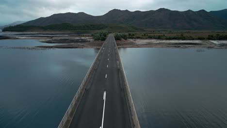 Vorwärts-Drohnenansicht-Einer-Leeren-Brücke-über-Dem-Lake-Burbury-Mit-Bergen-Im-Hintergrund-In-Tasmanien,-Australien-An-Einem-Bewölkten-Tag