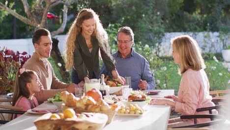 Video-of-happy-caucasian-parents,-daughter-and-grandparents-serving-food-at-table-before-meal