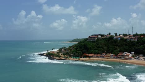 Rising-tilt-down-aerial-drone-wide-shot-of-the-tropical-famous-Baia-Formosa-beach-town-in-the-state-of-Rio-Grande-do-Norte,-Brazil-with-fishing-boats,-coastal-homes,-small-waves,-and-surfers