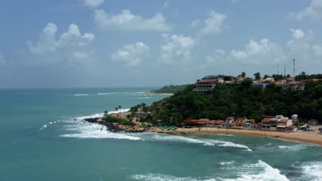 rising tilt down aerial drone wide shot of the tropical famous baia formosa beach town in the state of rio grande do norte, brazil with fishing boats, coastal homes, small waves, and surfers