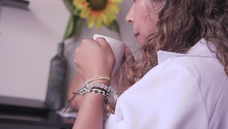 woman in profile drinking coffee from a cup with a sunflower in the background