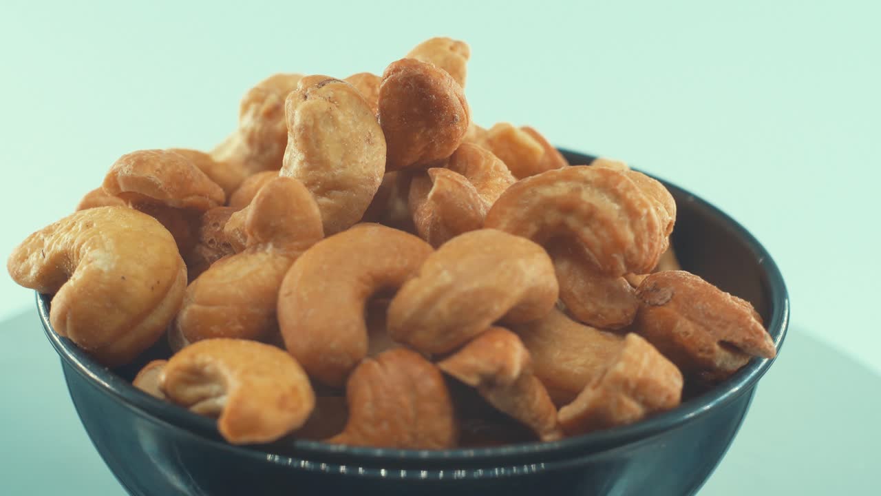 Et filmatisk nærbilde av en ristet, salt cashewnøtt i en blank, svart skål på et roterende stativ, sakte film, 4K.