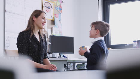 Schoolboy-presenting-a-gift-to-his-female-teacher-at-primary-school,-selective-focus,-side-view