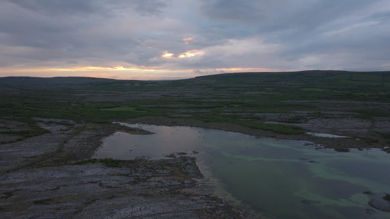 Nuvole si muovono sopra le acque riflettenti e i campi calcarei del Burren al crepuscolo. Ideale per documentari sulla natura o contenuti di viaggio.