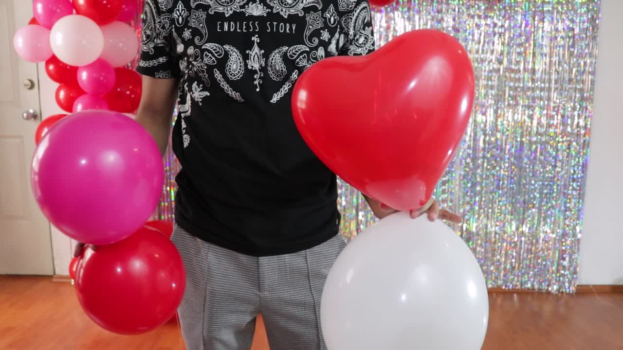 Man tying together Valentines day party balloons in decorated room