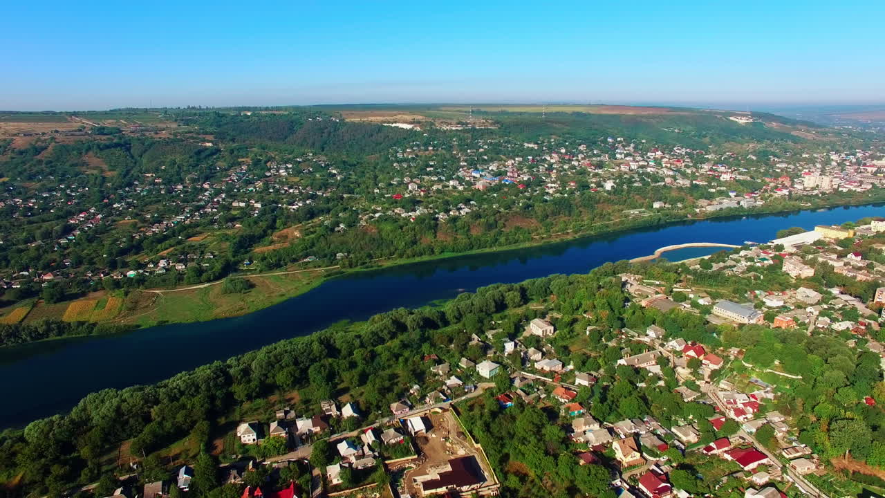 Dark blue river dividing the city into two parts. Dense architecture mixed with the beautiful greenery at backdrop of blue clear sky. Top view.