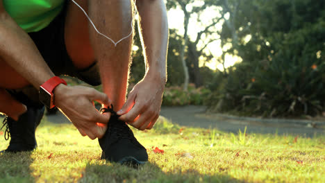 man tying his shoe laces while jogging in park