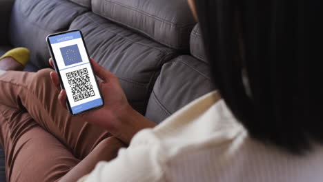 mujer en casa con un teléfono inteligente con certificado de vacunación contra la covid, bandera de la ue y código qr en la pantalla