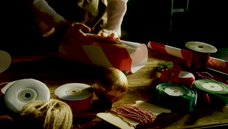 close up shot of the girl wrapping a gift for christmas on the flat table surface with other decorations in the view kept on the table