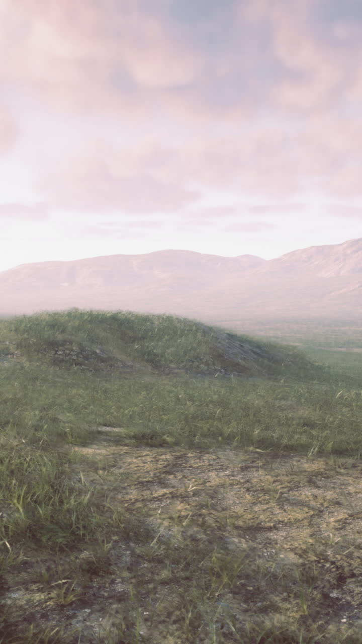 Vast grassy landscape with distant mountains under pastel sky at dusk