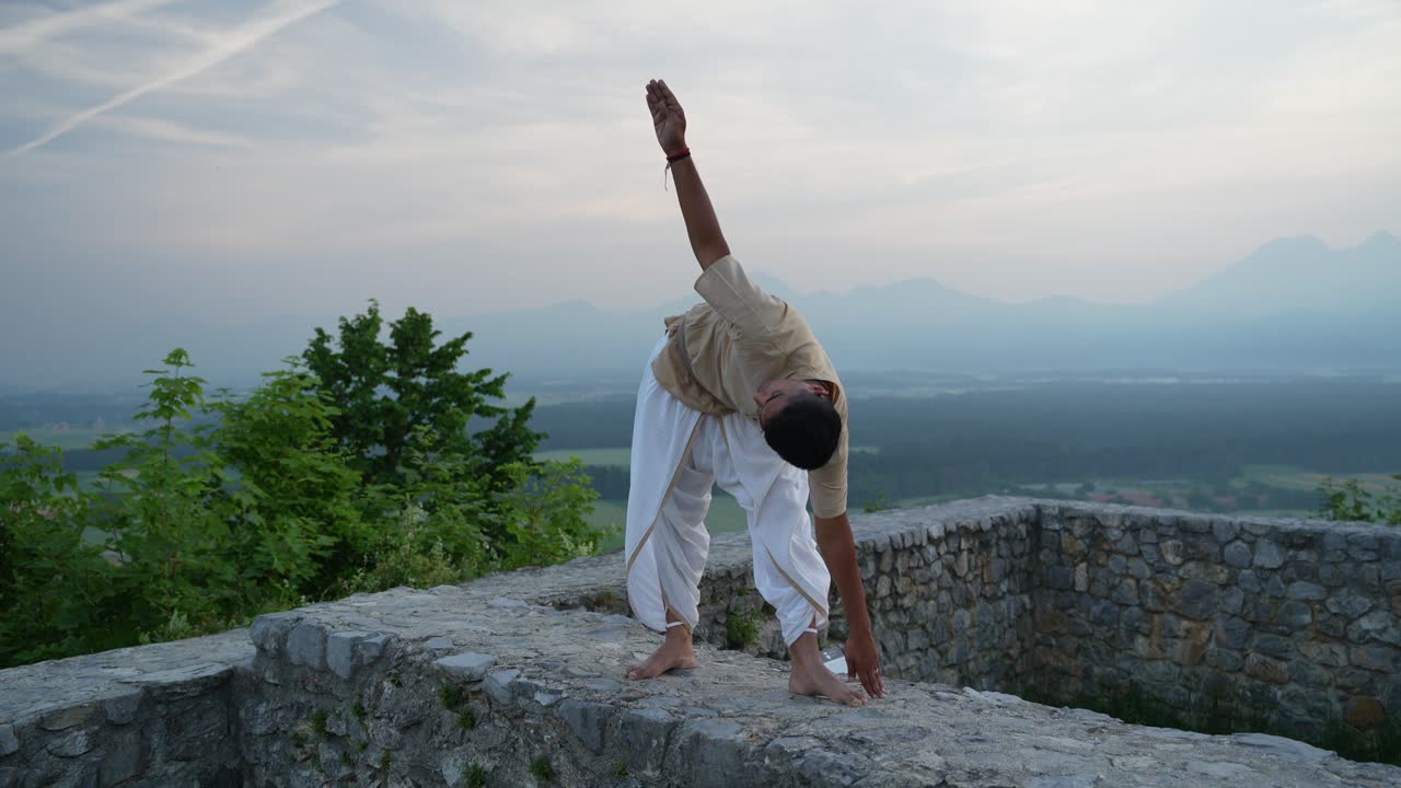 pose de yoga en la cima de la colina rodeada de campos y árboles al amanecer en la pared de piedra