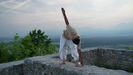 yoga pose at top of the hill surrounded with fields and trees at dawn on stone wall