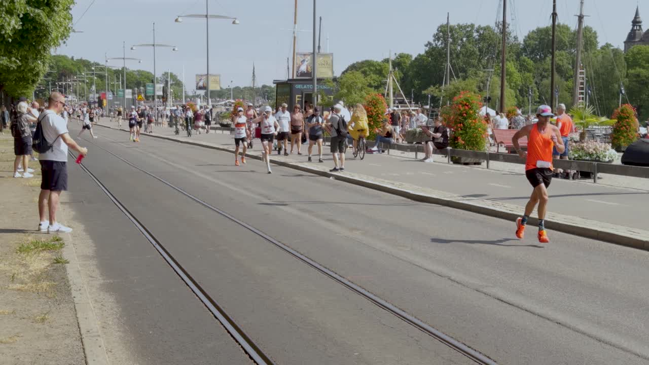 Runners race along sunny street at Stockholm Marathon as crowds cheer them on, slo-mo