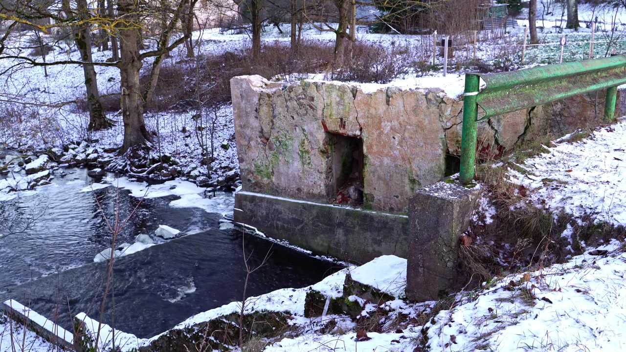 Icy river water flowing past a ruined concrete structure and snowy banks in a winter forest