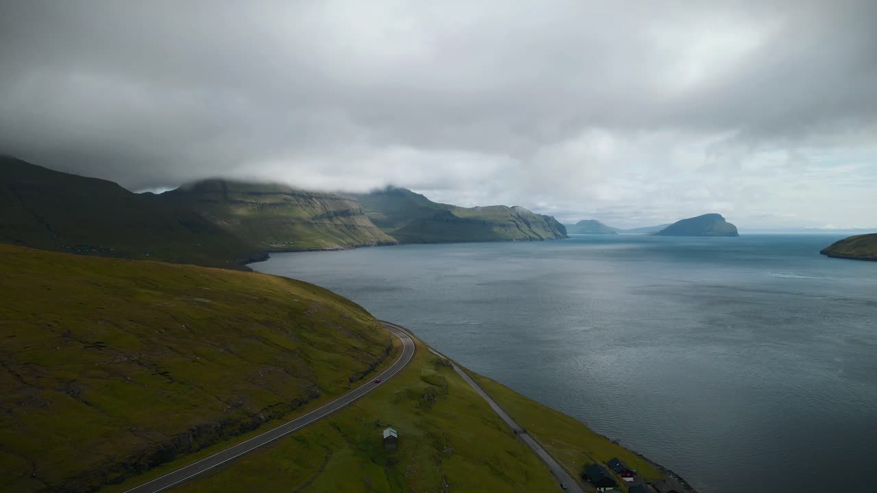 페로 제도 (faroe islands) 의 키비비크 (kvívík) 의 조용한 해안 풍경은 거친 산, 조용한 물, 휘어지는 도로, 구름이 많은 하늘이 북대서양의 이 환경에서 평화로운 분위기를 조성합니다.