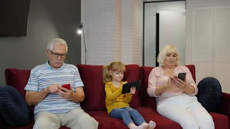 Senior-couple-grandparents-with-child-girl-granddaughter-using-digital-tablet,-mobile-phone