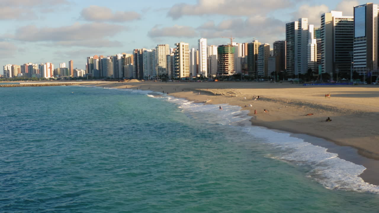 vista aérea desde el océano a los edificios frente a la playa, con algunas personas disfrutando, en un día soleado, fortaleza, brasil