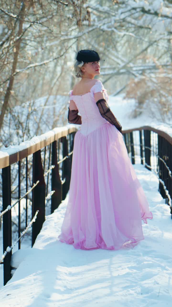 Elegant kvinne i rosa kjole går på snødekt bro om vinteren