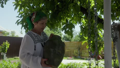 mujer rumana llevando una jarra de agua cerca del pozo - de cerca