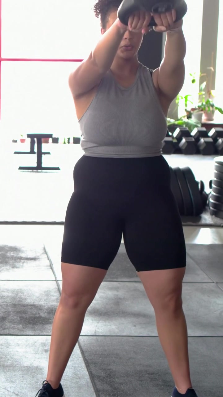 Video verticale: Donna in canotta e pantaloncini che esegue un hip hinge oscillando una kettlebell per la forza in studio.