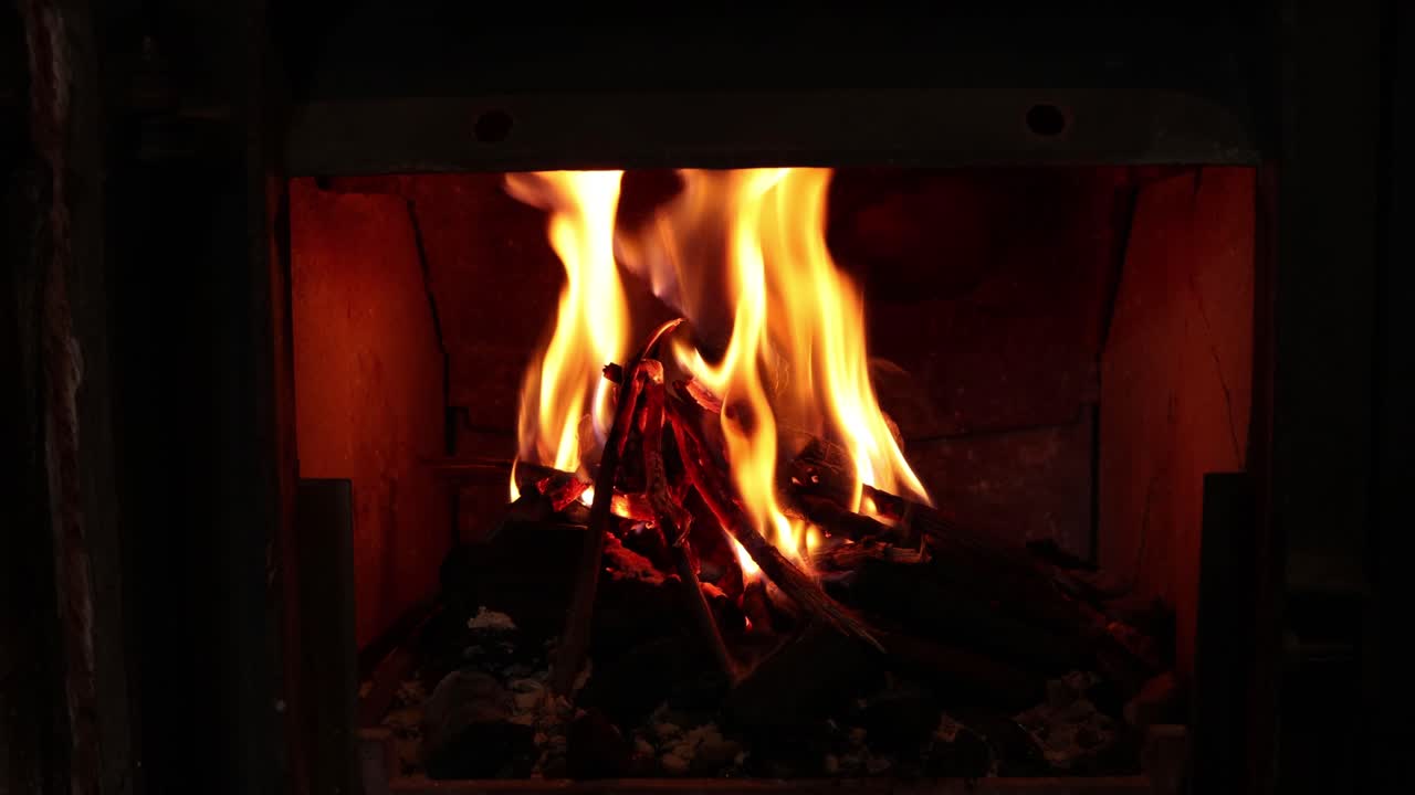 A wooden fire burning in a small fireplace with big flames and sparks. 4k shot.