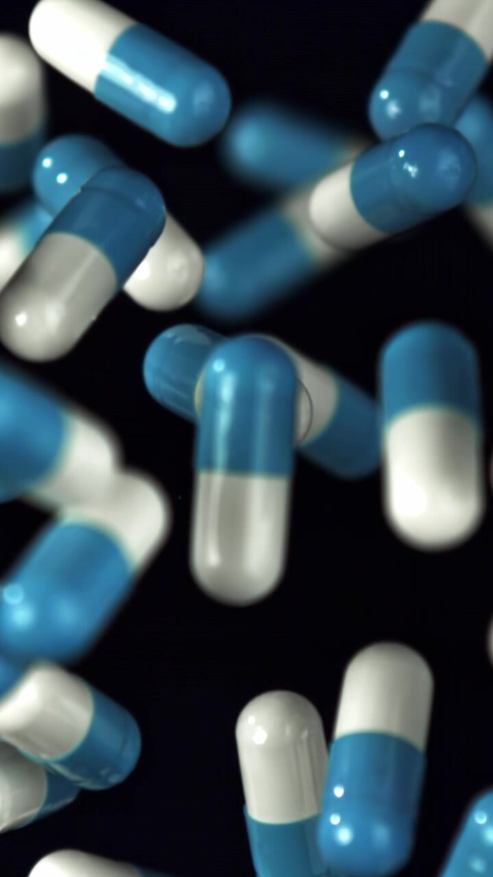 Blue and White Medical Capsules Floating in Slow Motion