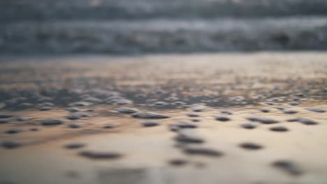 close-up of the shoreline with water bubbles reflecting the colours of the sunset during golden hour - trucking movement from left to right with blurry background