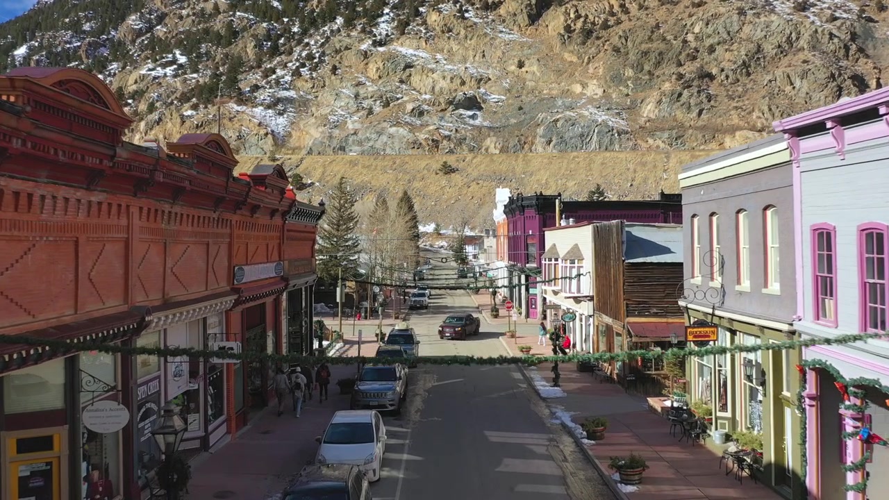 Ilmakuvaus dronella taaksepäin Coloradon yliopiston Boulderin kampuksen yllä, joka on lumen peitossa talviaamuna, ja taustalla eturivin vuoret ovat pilvien peitossa.