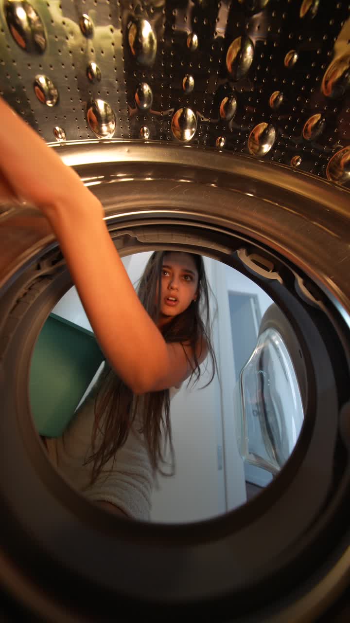Jovem mulher carregando roupas na máquina de lavar, vista interna