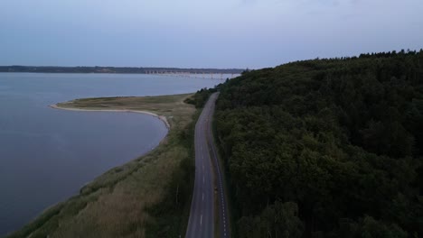 el dron vuela sobre la carretera y filma hacia el puente de sallingsund, con agua de un lado y bosque del otro