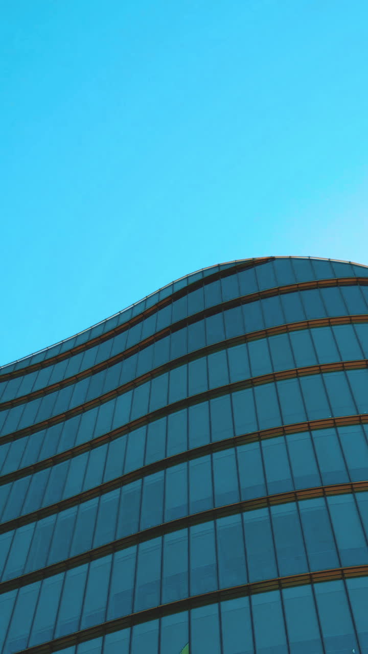 Edificio moderno de cristal curvo con reflejos que se elevan hacia el cielo azul