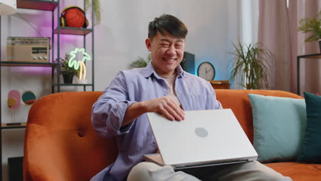 Man-guy-freelancer-sitting-on-couch-closing-laptop-pc-after-finishing-work-in-living-room-at-home