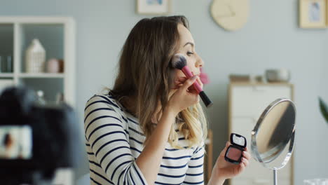 hermosa bloguera de belleza grabando un video tutorial de maquillaje y enseñando cómo aplicar rubor en las mejillas 1