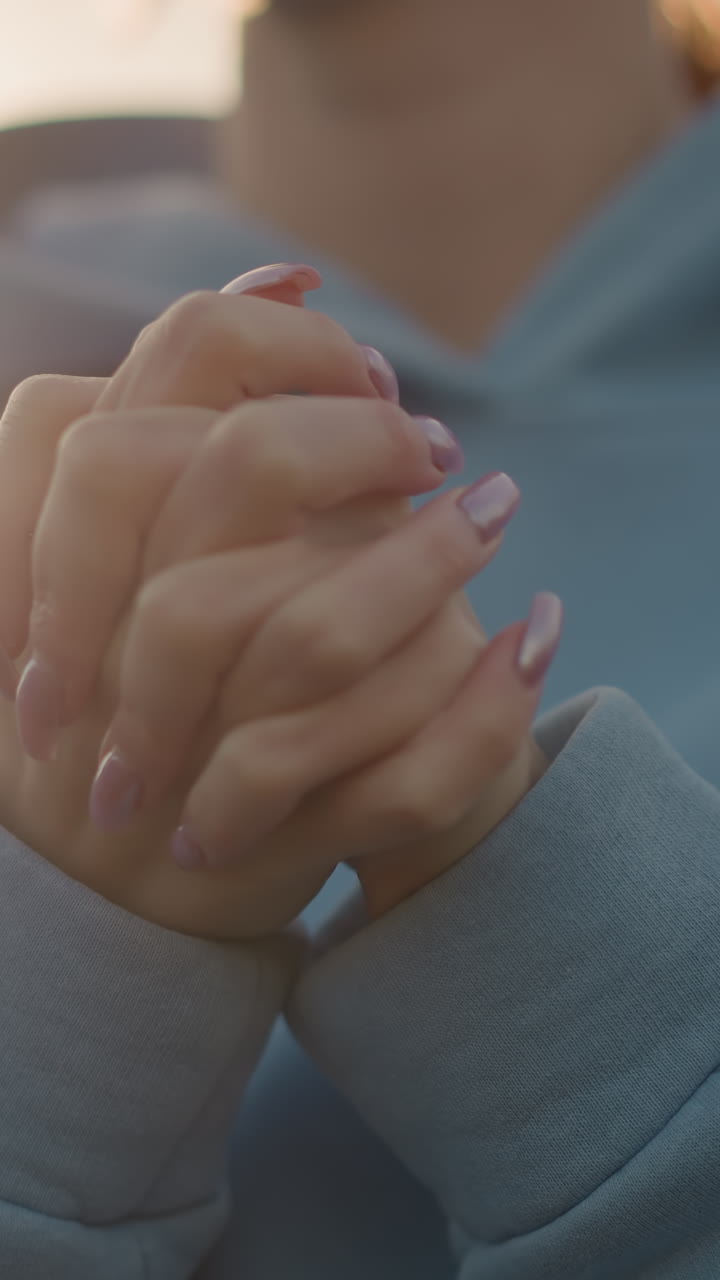 primer plano de una mujer con uñas pulidas realizando una torsión de la muñeca, con suéter azul, mostrando las manos en foco con un fondo suave, manos elegantes y movimiento de las muñecas en la rutina de fitness