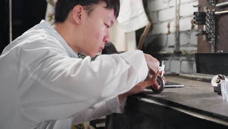 student in white lab coat picks up boris, uses vernier caliper to measure diameter on workbench in mechanical store, background includes tools, industrial equipment, and tablet for recording data