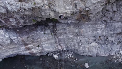 downwards aerial shot of a man crossing a steep river gorge with a fixed cable and sliding platform in helambu, nepal