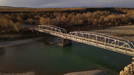 long aerial video in 4k of an old steel bridge in rural alberta, canada during fall season. drone orbiting around the structure that connects the banks of old man river while also ascending