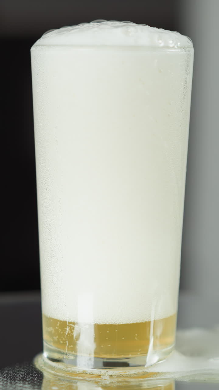 la espuma de cerveza pálida cae juguetonamente en cascada sobre la superficie reflectante y sombreada de una mesa moderna, sugiriendo un entorno íntimo para un momento refrescante.